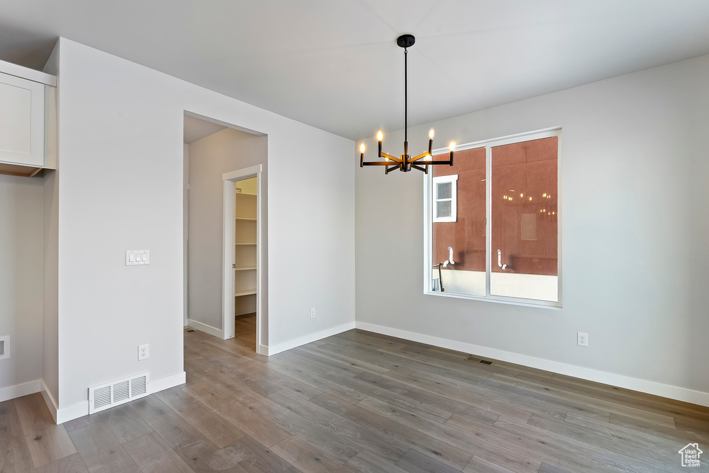 Unfurnished dining area featuring visible vents, baseboards, a notable chandelier, and wood finished floors