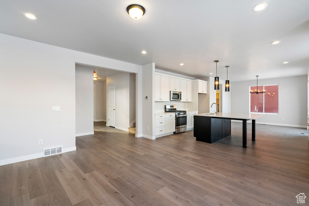 Kitchen with an inviting chandelier, an island with sink, white cabinets, visible vents, and stainless steel appliances
