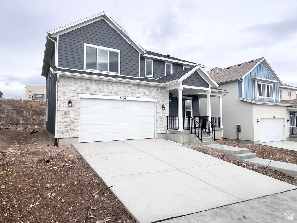 View of front facade featuring an attached garage, concrete driveway, covered porch, and stone siding