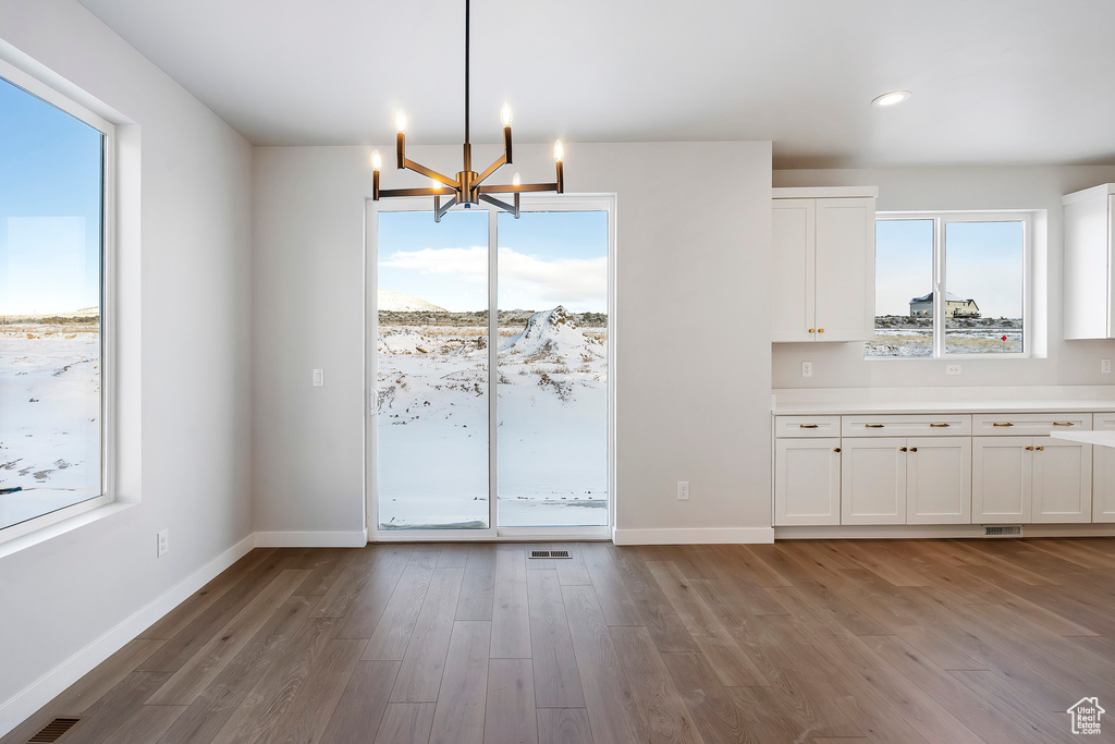 Unfurnished dining area featuring recessed lighting, baseboards, an inviting chandelier, and wood finished floors