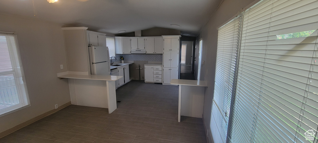 Kitchen with baseboards, light countertops, freestanding refrigerator, white cabinetry, and vaulted ceiling