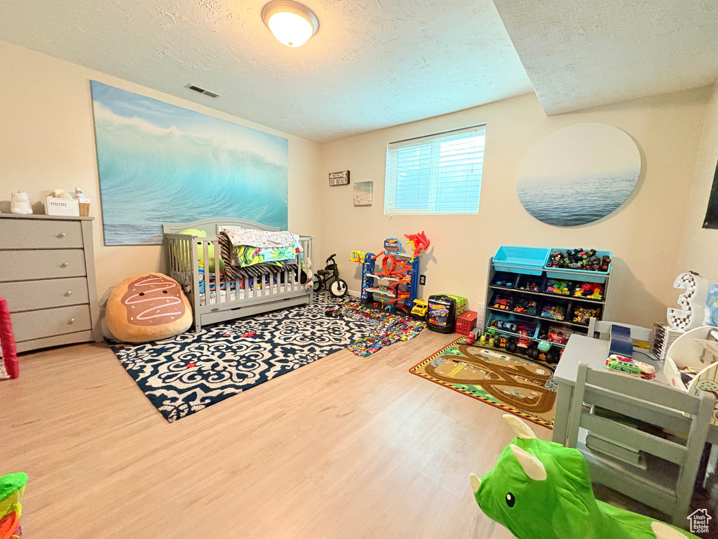 Bedroom with a crib, visible vents, a textured ceiling, and wood finished floors