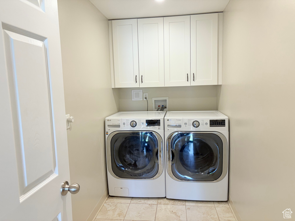Washroom with cabinet space, light tile patterned floors, baseboards, and separate washer and dryer