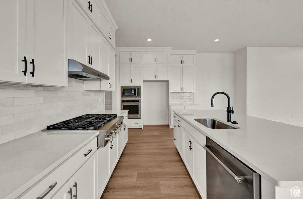 Kitchen with a sink, stainless steel appliances, under cabinet range hood, recessed lighting, and light wood-style floors