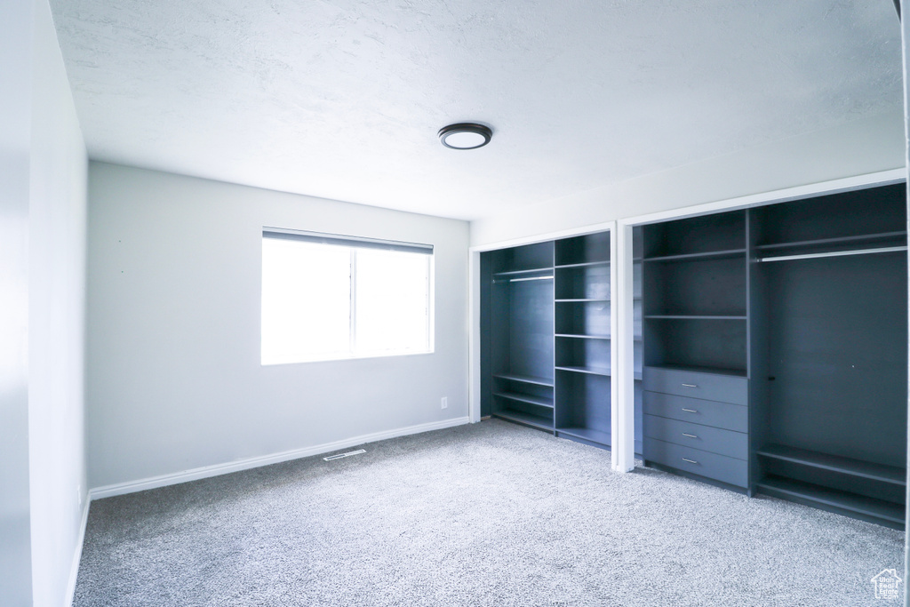 Unfurnished bedroom featuring visible vents, baseboards, carpet floors, and two closets