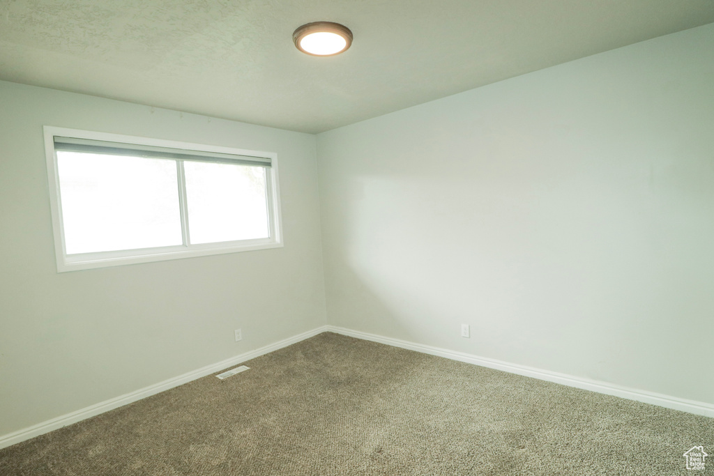 Empty room with carpet floors, visible vents, and baseboards