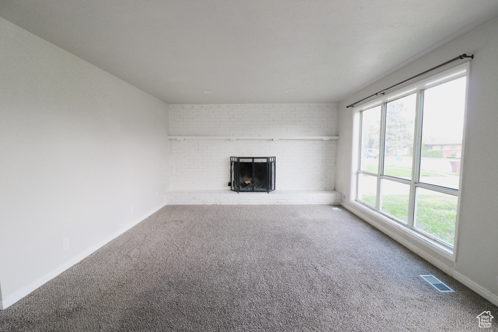Unfurnished living room with a fireplace, carpet floors, visible vents, and baseboards