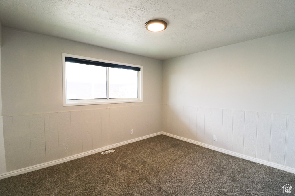 Unfurnished room featuring wooden walls, visible vents, dark carpet, and a textured ceiling