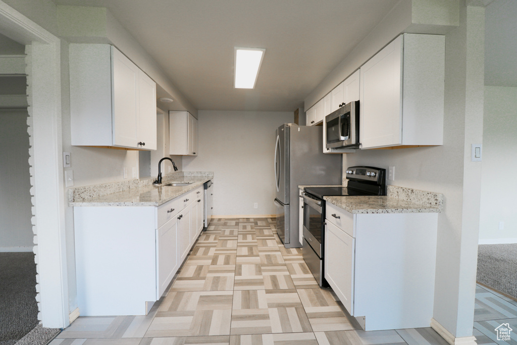 Kitchen featuring white cabinets, stainless steel appliances, light stone countertops, and a sink