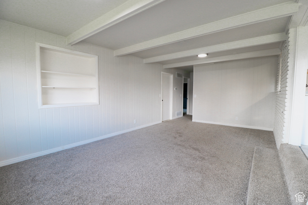 Empty room featuring beamed ceiling, carpet floors, and baseboards