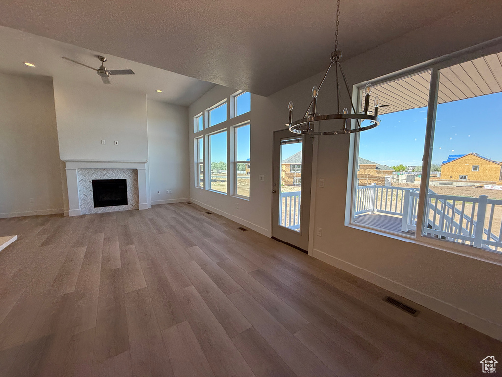 Unfurnished living room featuring wood finished floors, baseboards, a chandelier, ceiling fan, and a fireplace