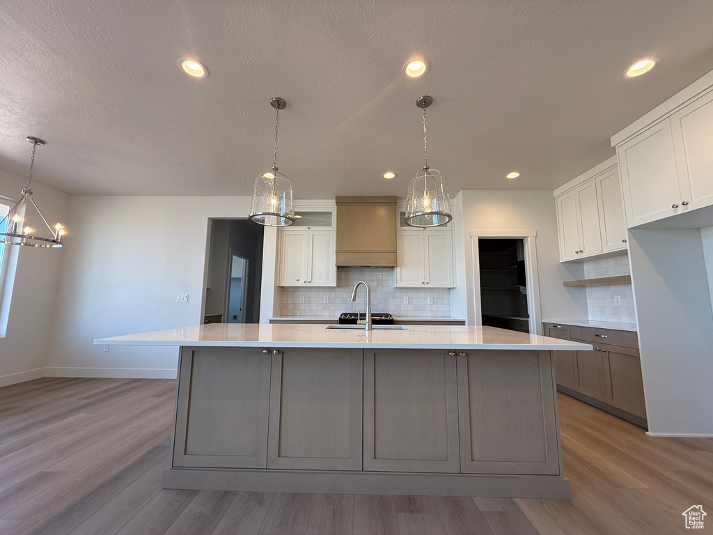 Kitchen featuring wood finished floors, tasteful backsplash, light countertops, white cabinets, and recessed lighting