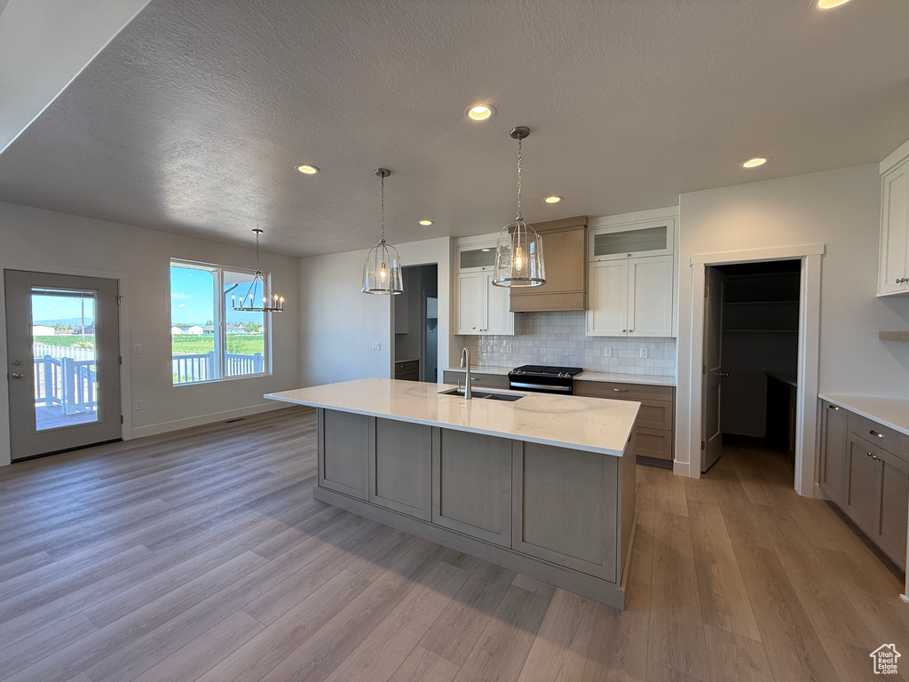 Kitchen featuring light wood-type flooring, backsplash, a sink, glass insert cabinets, and custom exhaust hood