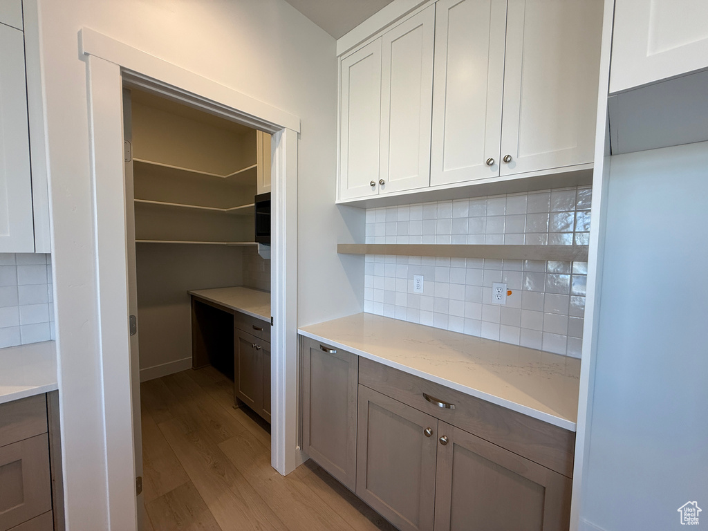 Kitchen featuring open shelves, light wood-type flooring, tasteful backsplash, and light stone counters