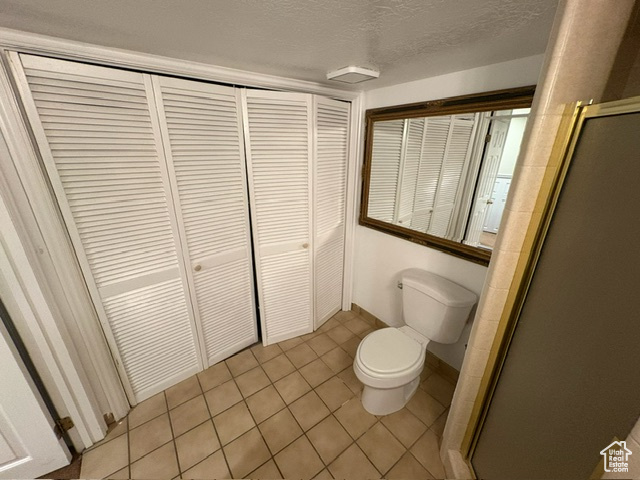 Bathroom featuring toilet, a closet, a stall shower, tile patterned flooring, and a textured ceiling