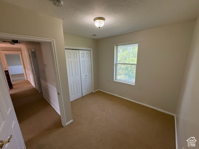 Unfurnished bedroom featuring light colored carpet, a closet, baseboards, and a textured ceiling