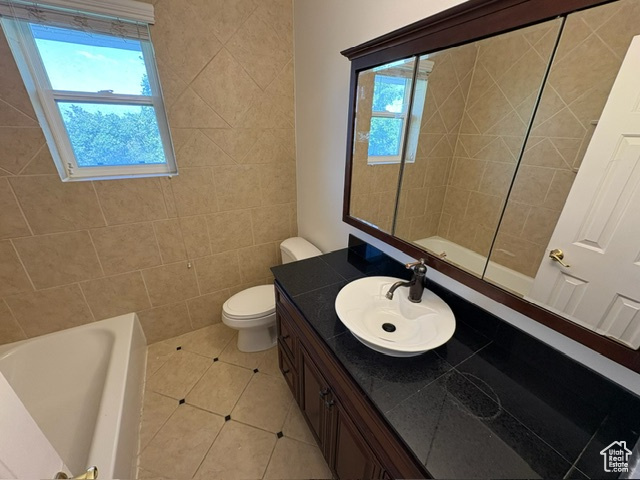 Full bathroom featuring healthy amount of natural light, a bathtub, vanity, tile patterned floors, and tile walls