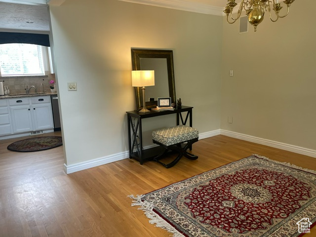 Hallway featuring a chandelier, light wood-style flooring, baseboards, ornamental molding, and a sink
