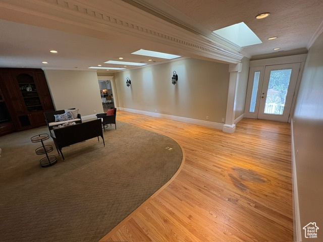 Living area with crown molding, a skylight, light wood-style floors, baseboards, and recessed lighting