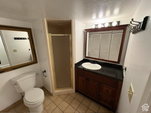 Bathroom featuring toilet, a stall shower, tile patterned floors, vanity, and a textured ceiling