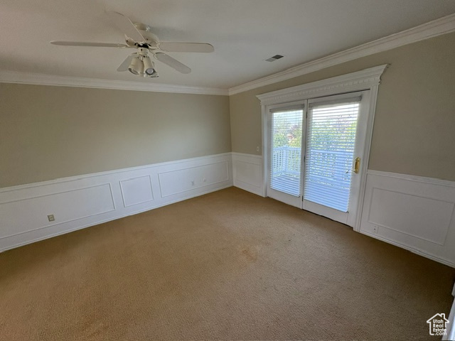 Spare room with ornamental molding, wainscoting, a ceiling fan, carpet flooring, and a decorative wall