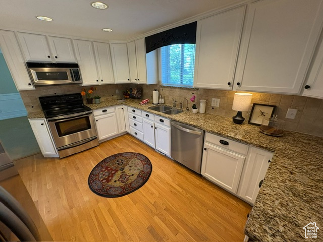 Kitchen with stainless steel appliances, a sink, light wood-style flooring, white cabinets, and recessed lighting