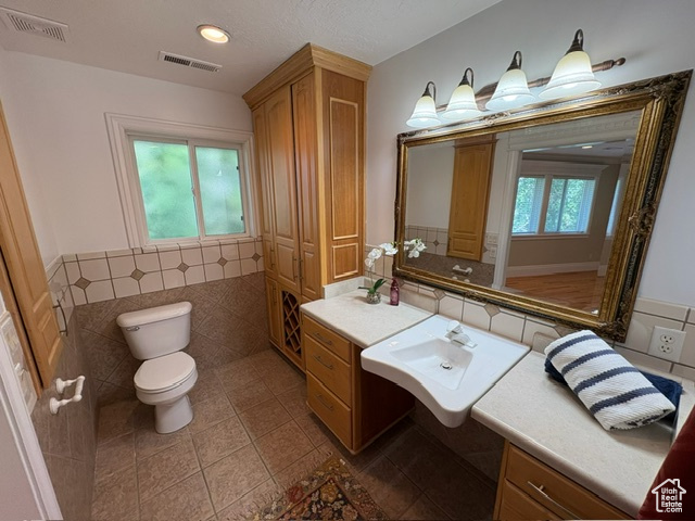 Bathroom featuring toilet, tile patterned flooring, tile walls, and a sink