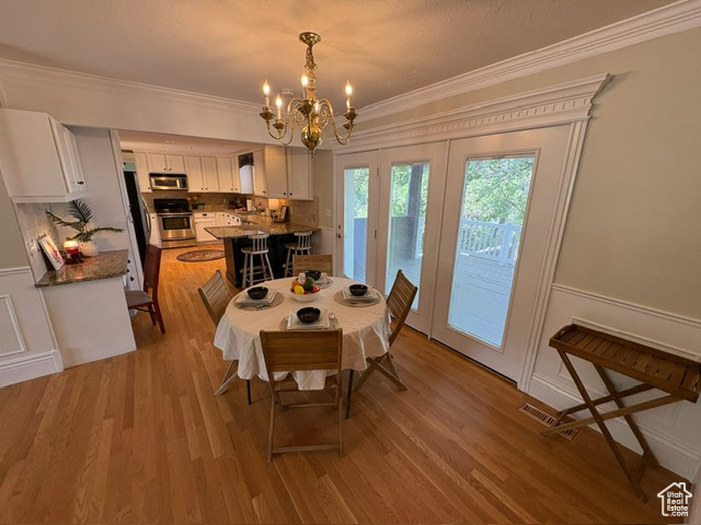 Dining area featuring crown molding, a chandelier, light wood finished floors, wainscoting, and a decorative wall