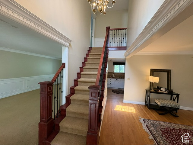 Staircase featuring a chandelier, crown molding, and wood finished floors
