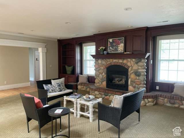 Living area featuring crown molding, a stone fireplace, recessed lighting, baseboards, and light wood-style flooring