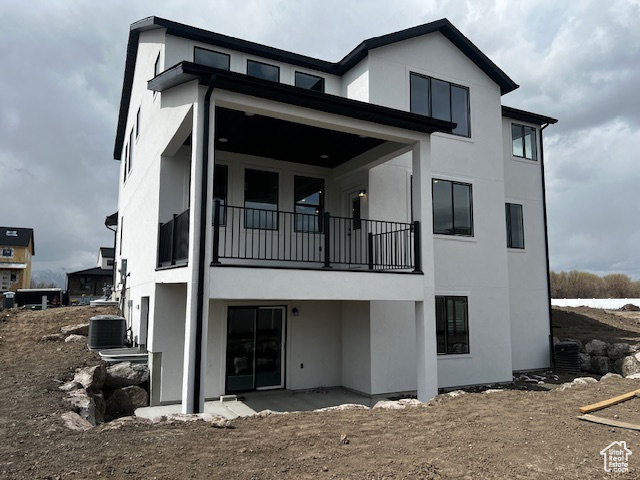Rear view of house featuring cooling unit, a patio area, stucco siding, and a balcony