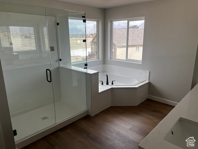 Bathroom featuring a shower stall, a bath, wood finished floors, a sink, and baseboards