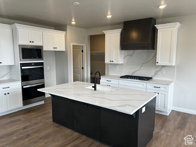 Kitchen featuring white cabinetry, stainless steel microwave, a sink, premium range hood, and black cooktop