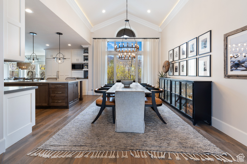 Dining space with baseboards, a notable chandelier, high vaulted ceiling, dark wood-type flooring, and ornamental molding