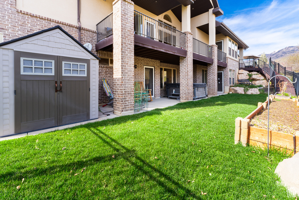 Exterior space featuring a patio area, a lawn, an outbuilding, brick siding, and a storage unit