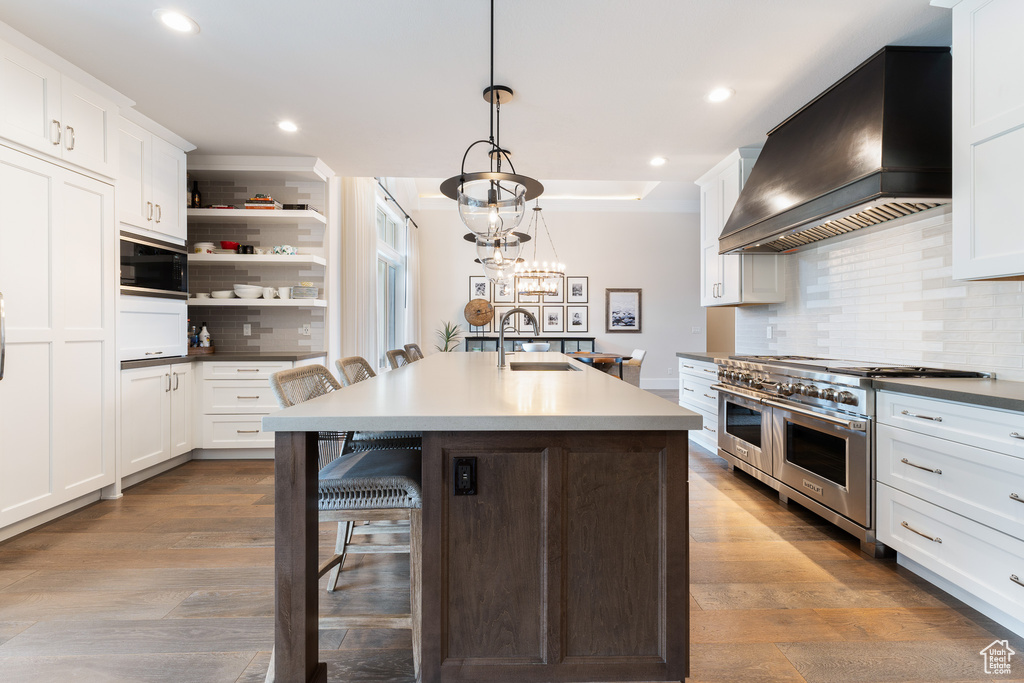 Kitchen featuring built in microwave, a sink, tasteful backsplash, custom range hood, and range with two ovens