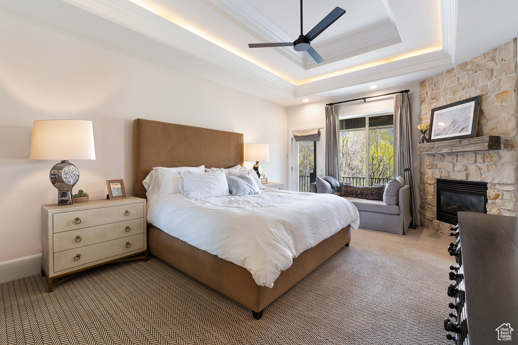 Carpeted bedroom featuring a raised ceiling, access to exterior, crown molding, a fireplace, and ceiling fan