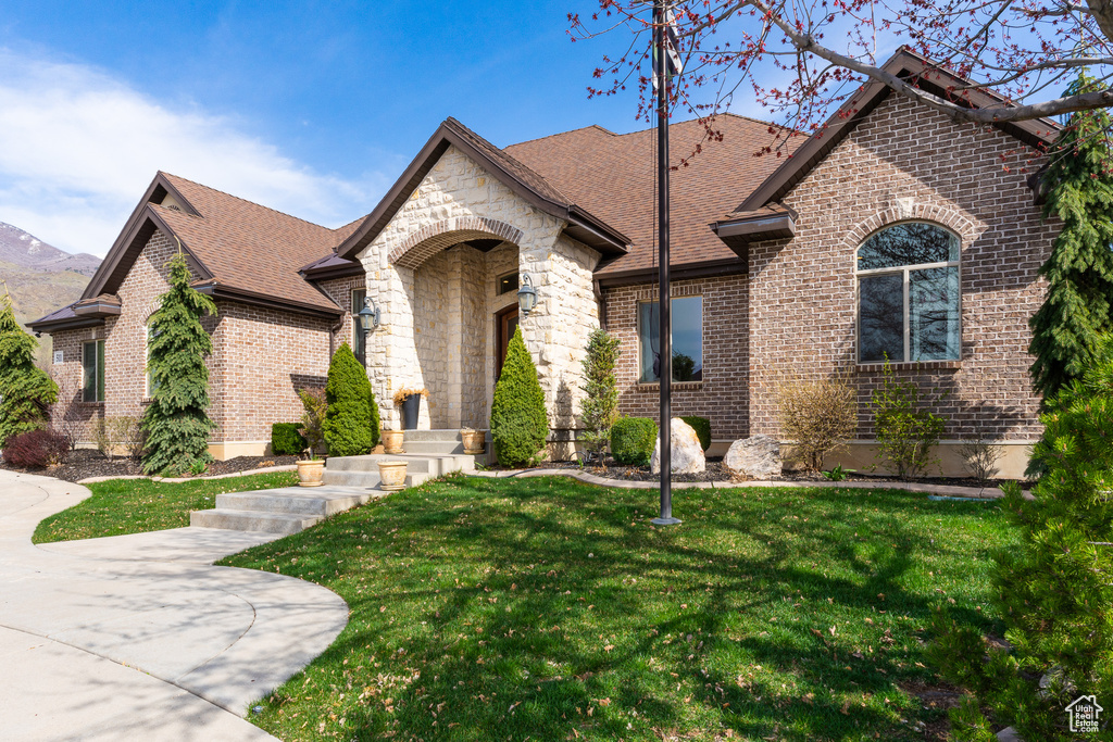 French country style house with brick siding, roof with shingles, stone siding, and a front lawn