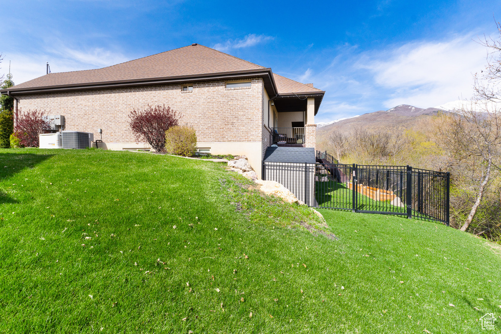View of side of property featuring a lawn, central air condition unit, fence, a mountain view, and brick siding