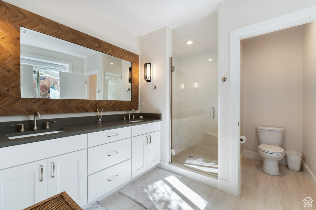Full bath featuring toilet, a sink, double vanity, and a stall shower