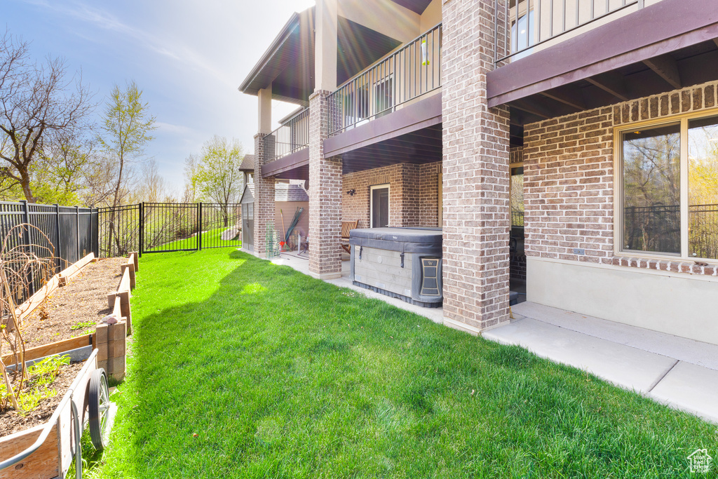 View of yard featuring a garden, a hot tub, a fenced backyard, and a balcony