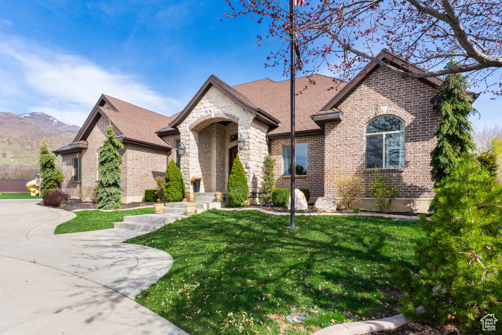 View of front of property with brick siding, a shingled roof, a front lawn, and a mountain view