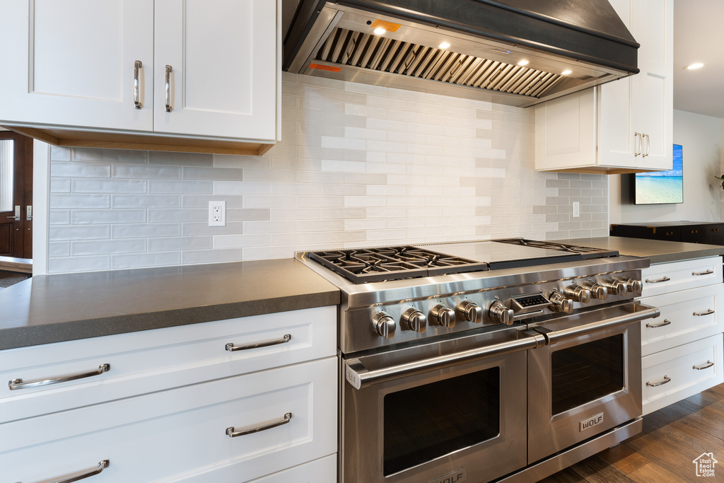 Kitchen with premium range hood, decorative backsplash, dark countertops, and double oven range