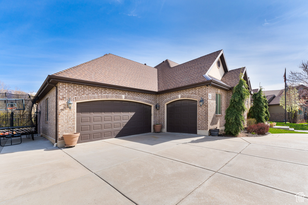 View of property exterior with concrete driveway, brick siding, a shingled roof, and a garage
