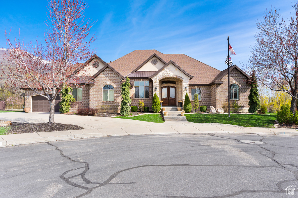 View of front of property featuring a front lawn, driveway, a shingled roof, a garage, and brick siding