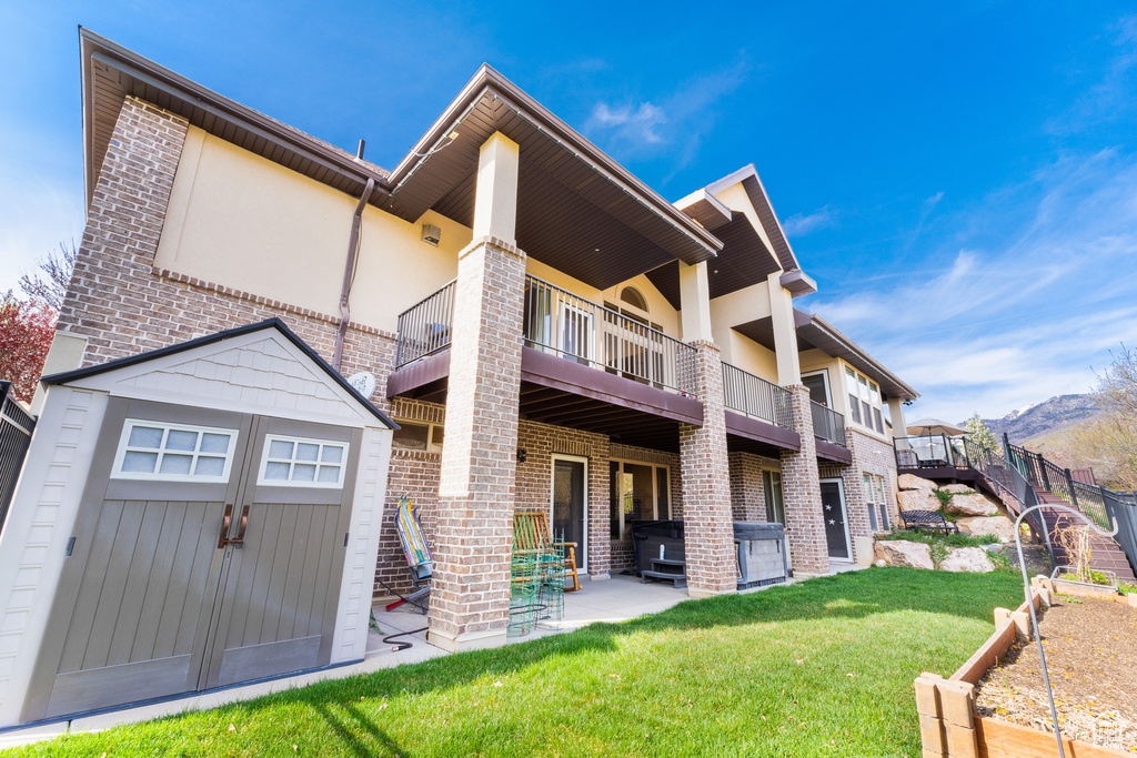 Rear view of house with a balcony, a lawn, an outdoor structure, a patio, and a storage unit