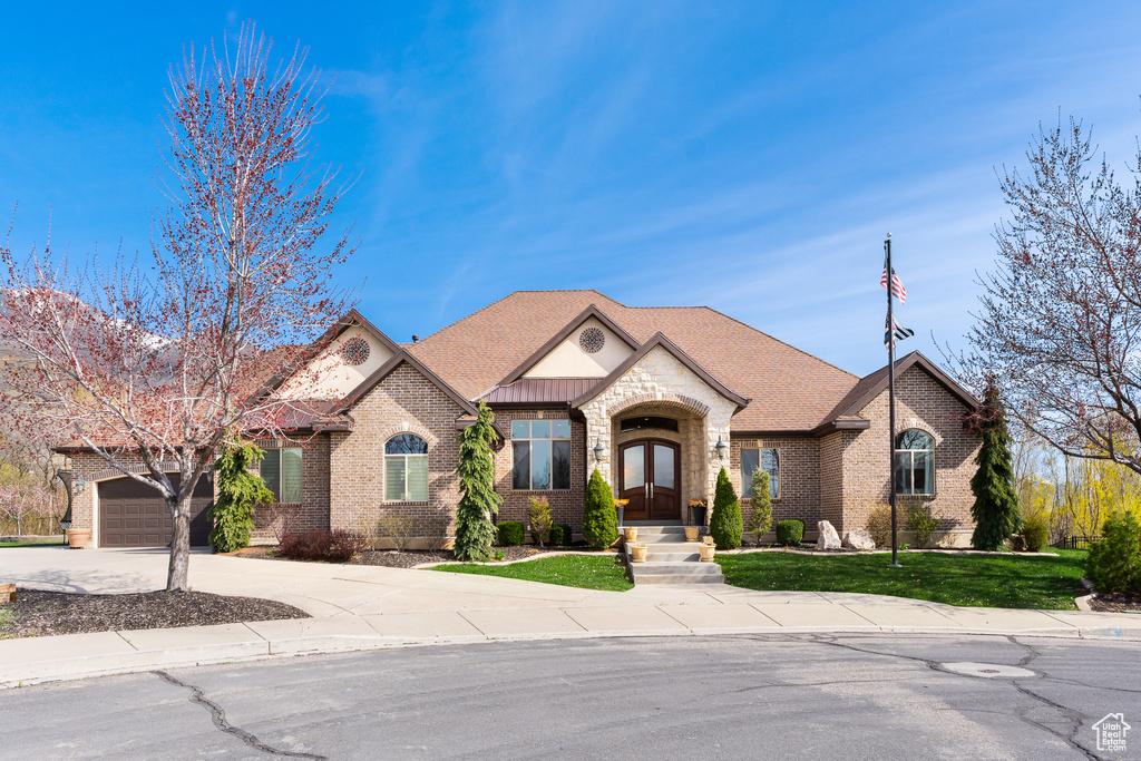 View of front of house with driveway, a shingled roof, french doors, an attached garage, and brick siding