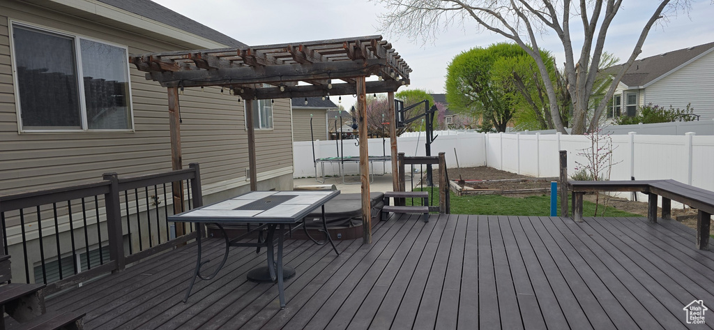 Wooden terrace with a fenced backyard, a trampoline, outdoor dining area, and a pergola