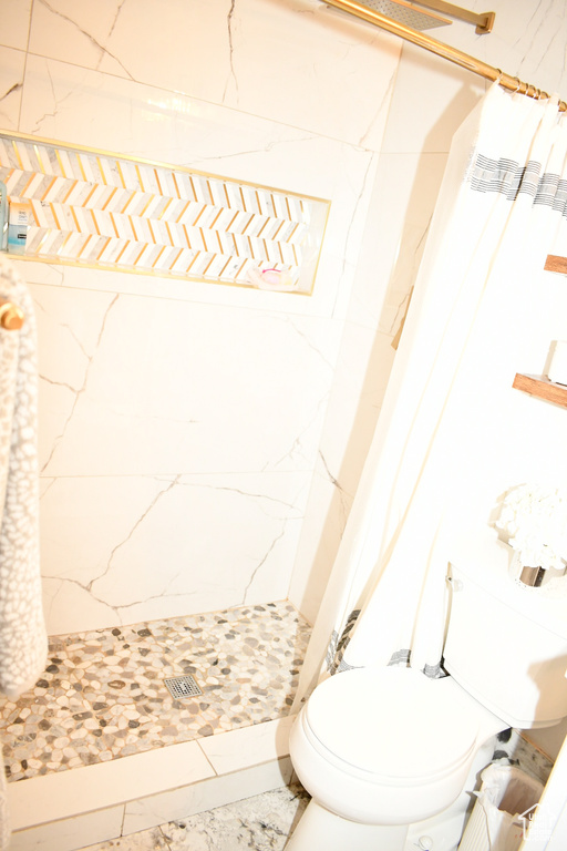 Bathroom featuring toilet, a shower stall, and marble finish floor