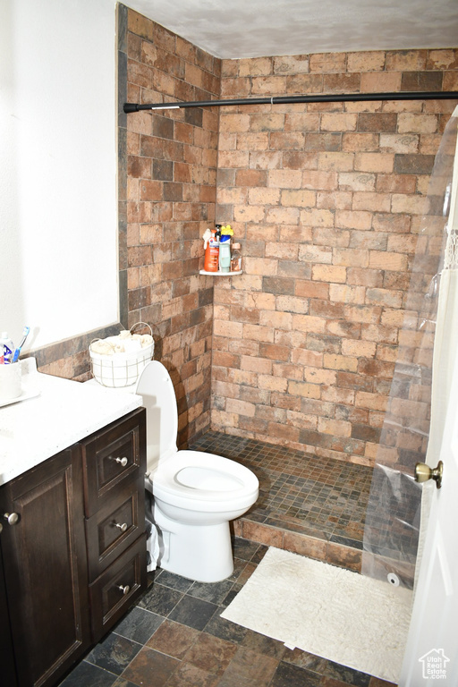 Full bath featuring toilet, stone tile floors, vanity, and tiled shower
